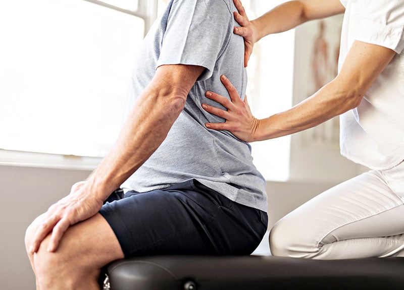 A physical therapist's hands on an older man's back, indicating a massage or adjustment.