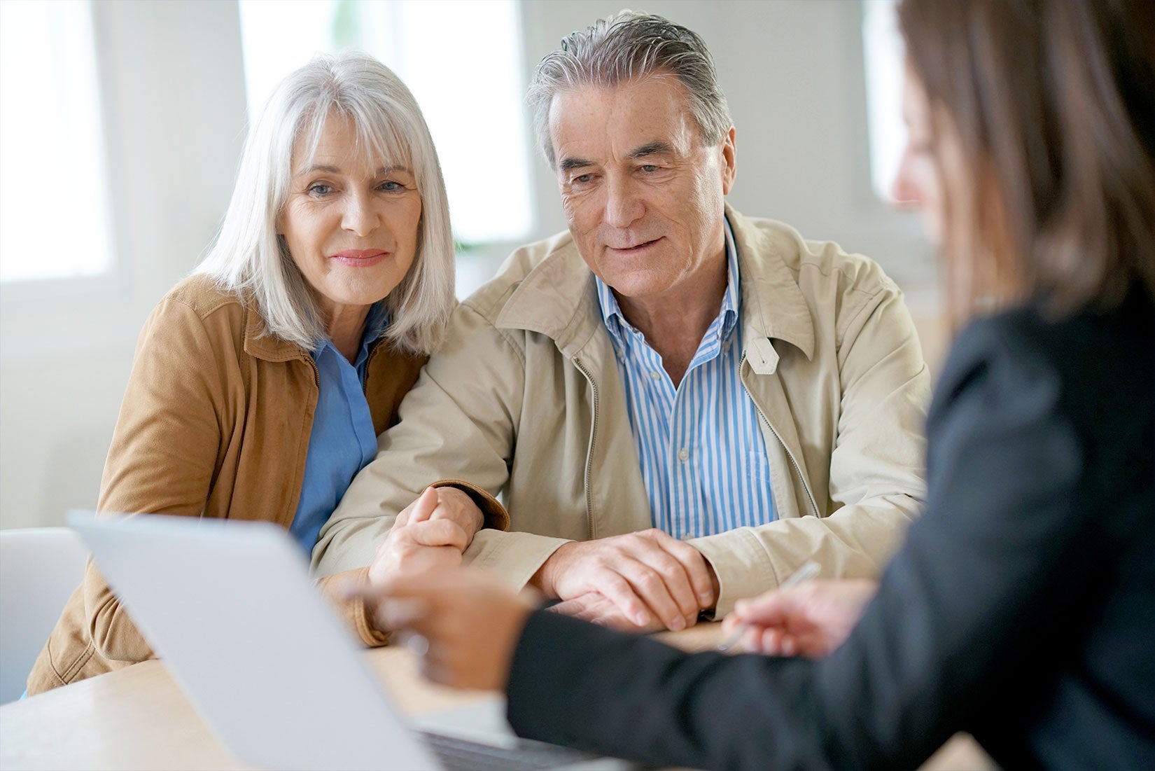 An older couple sitting at a desk with a financial advisor pointing at a laptop.