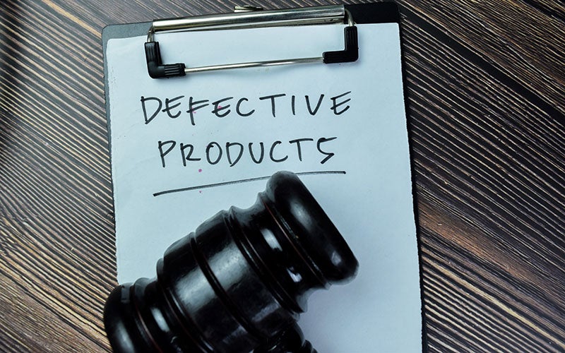 A gavel resting on a clipboard with DEFECTIVE PRODUCTS written on it.