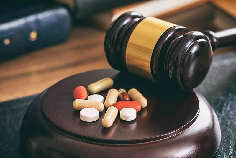 A judge's gavel lies on its side, with assorted pills and capsules scattered on its base.