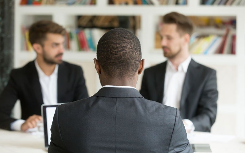 View from behind a person's head looking at two men in suits across a table.